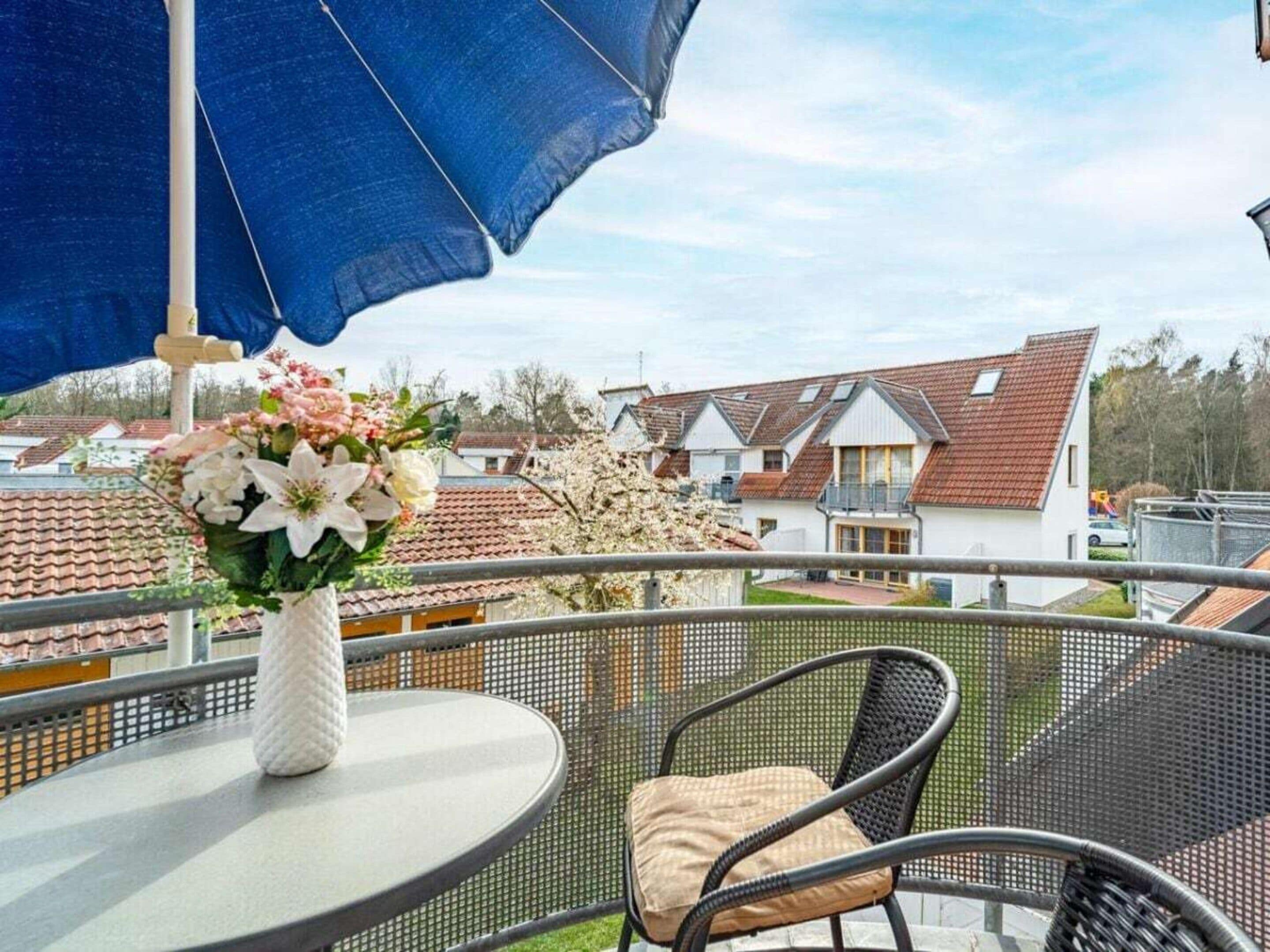 A balcony with a table, chairs, and a blue umbrella.