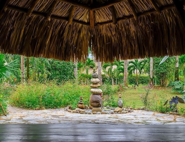 A thatched-roof structure surrounded by a garden with a stone pathway and a stack of stones.