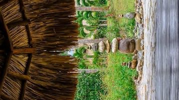 A thatched-roof structure with a garden pathway leading to a stone wall.