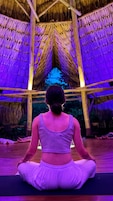 Una persona sentada en posición meditativa dentro de una estructura con techo de paja.
