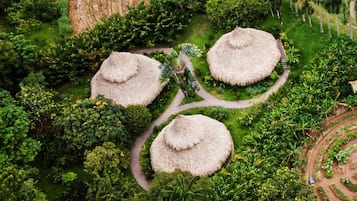 Ein kreisförmiges Gartenlayout mit drei Gebäuden, deren Dächer mit Schilf gedeckt sind, umgeben von üppigem Grün und einem gewundenen Weg.