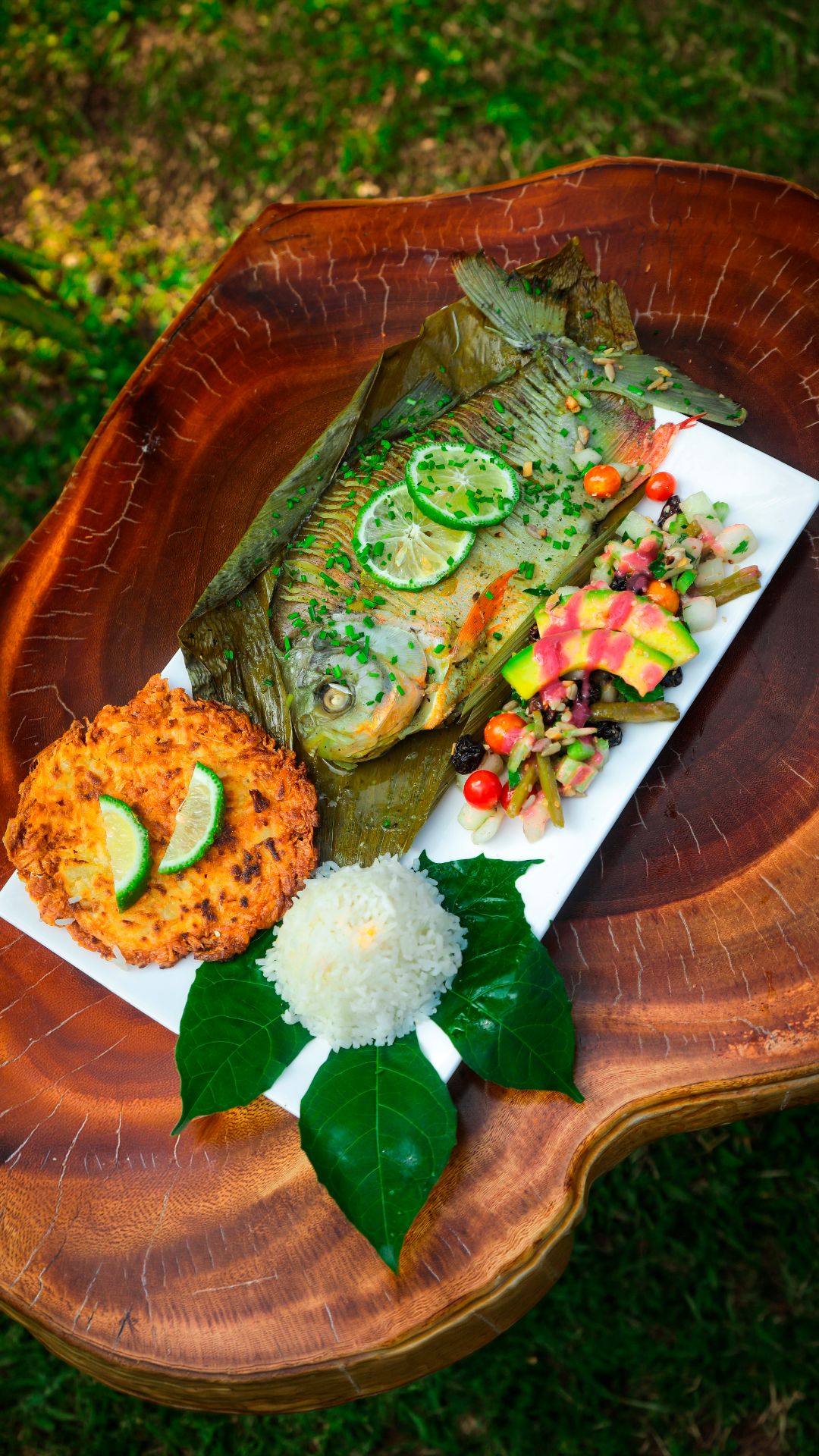 Un plato de comida con un pescado entero, arroz y un acompañamiento sobre una tabla de madera.