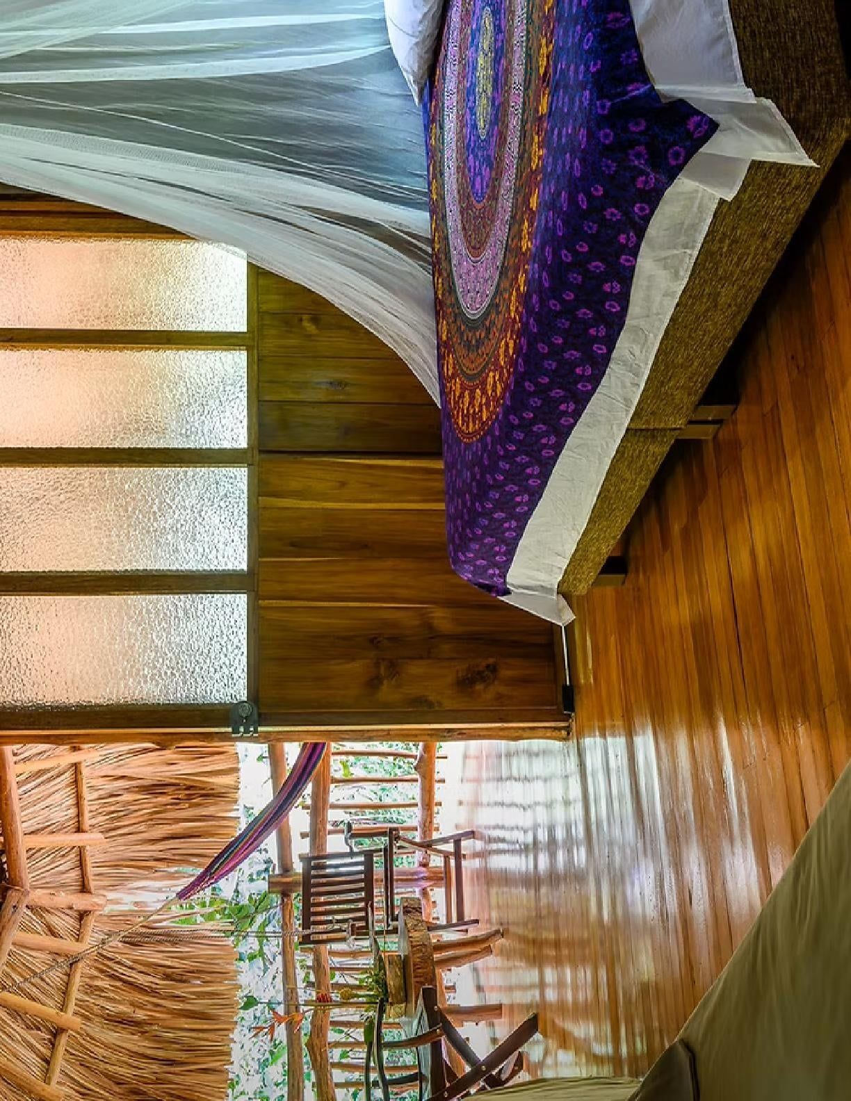 Una habitación con piso de madera, un ventanal con vidrio esmerilado y una cama con manta estampada.