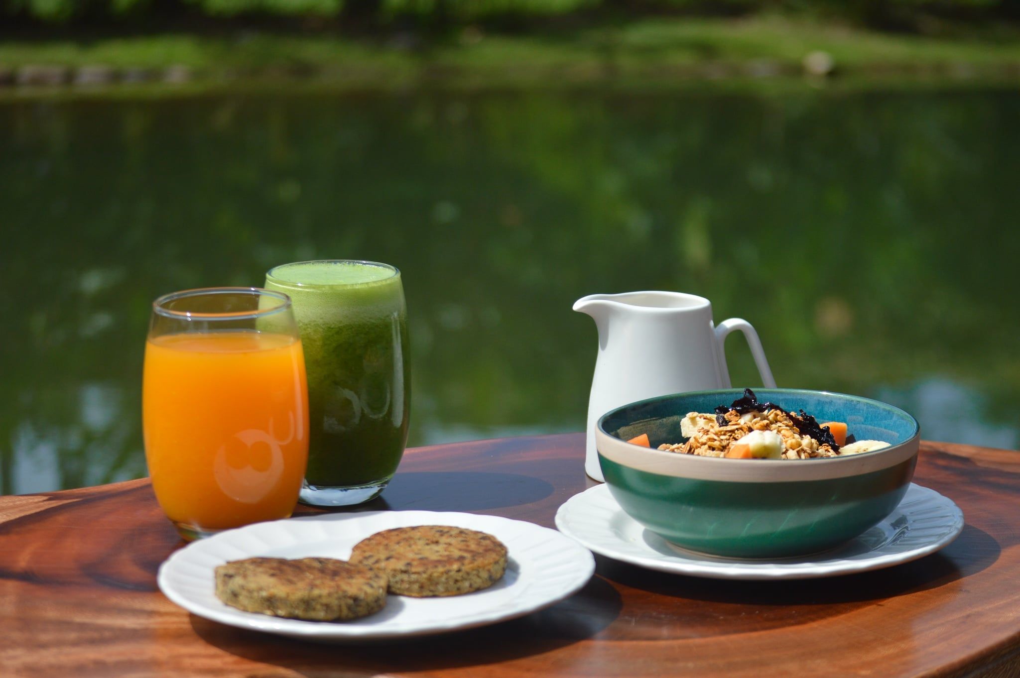Desayuno con un tazón de cereales, dos vasos de jugo, una jarra y un plato de galletas.