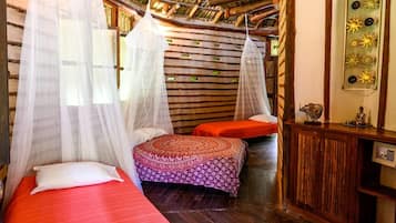 A room with two beds, each with a canopy, a small table with decorative items, and a wooden ceiling.