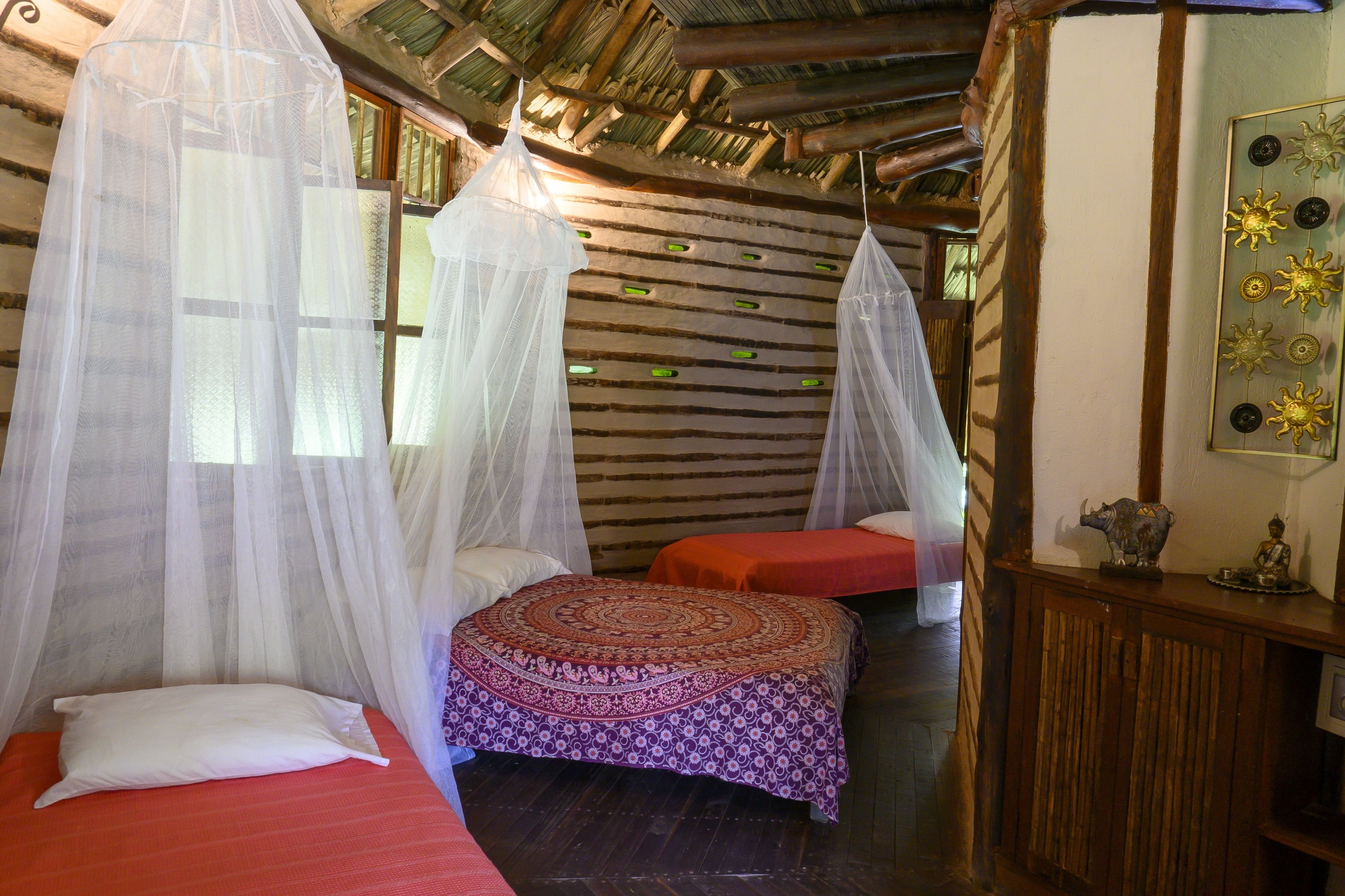 A room with two beds, each with a canopy, a small table with decorative items, and a wall with a unique pattern.