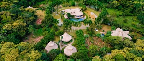 Vista aérea de un resort con estructuras de techo de paja, una piscina y un bosque denso circundante.