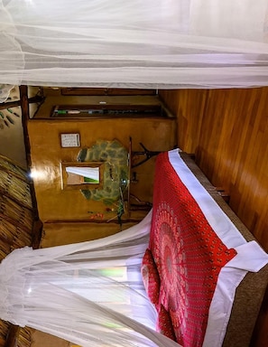 A room with a bed under a canopy, a wooden desk, and a stone wall.