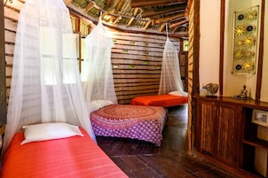 Una habitación con dos camas, cada una con dosel, una mesita con adornos y un techo de madera.