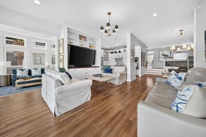 A spacious living room with a large flat-screen TV, a sofa, a coffee table, and a dining area with a kitchen in the background. - A Place To Land 3 Bedroom Villa (Georgetown)