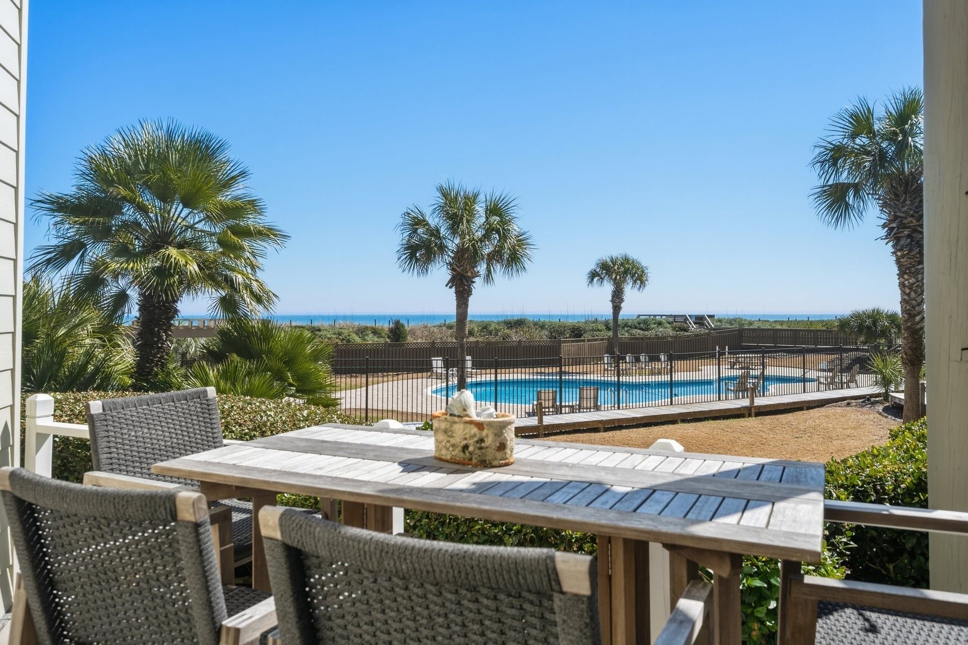 A pool area with a view of the ocean, surrounded by palm trees and a wooden fence.