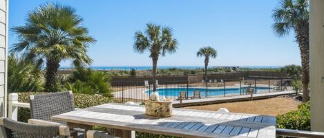 A pool area with a view of the ocean, surrounded by palm trees and a wooden fence.