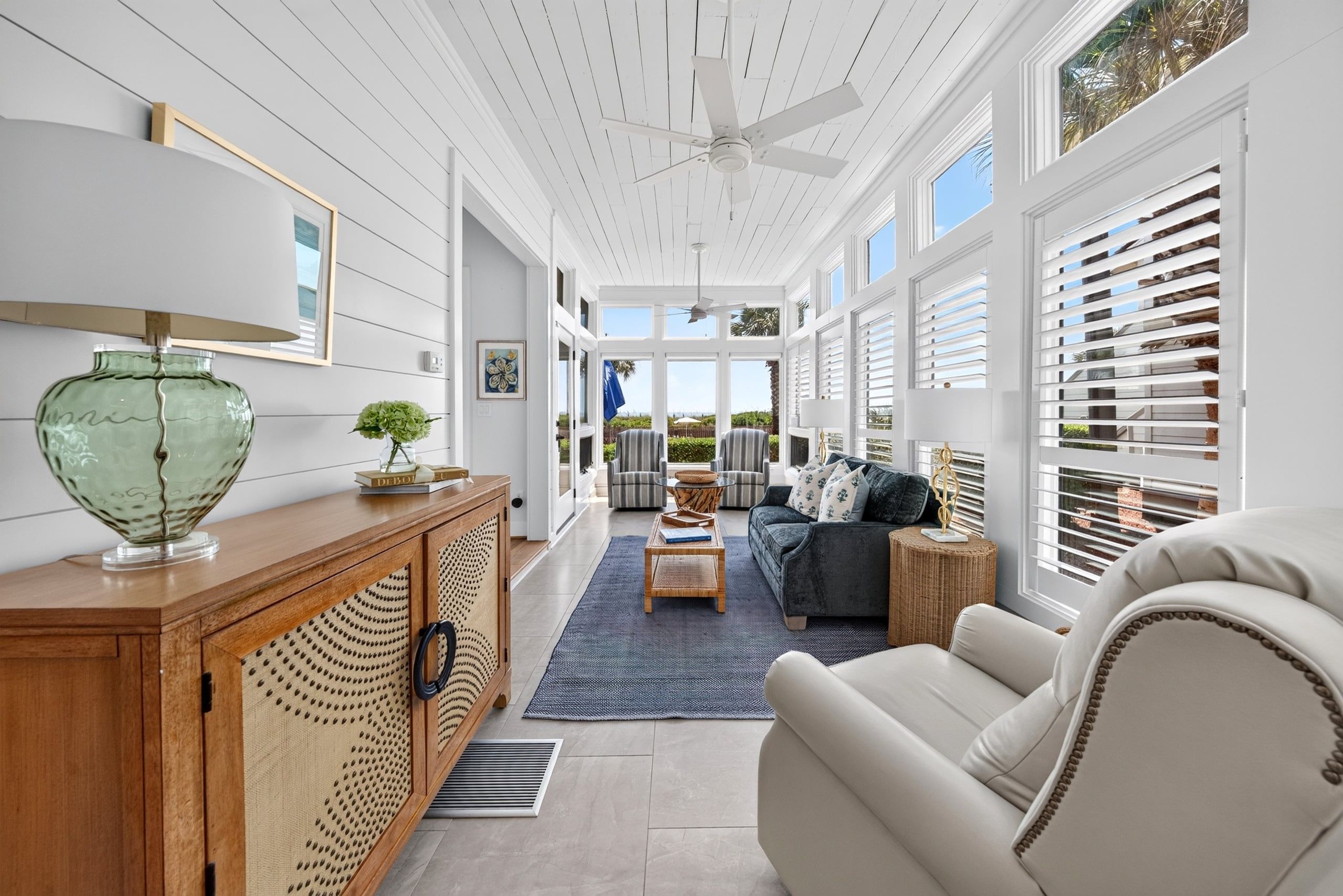 A spacious living area with a ceiling fan, a large window with blinds, a sofa, and a coffee table.