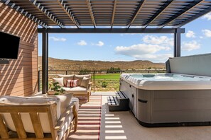 An outdoor patio with a hot tub, seating area, and a view of a hilly landscape. - The Isle Retreat 6 Bedroom Townhouse (Washington)