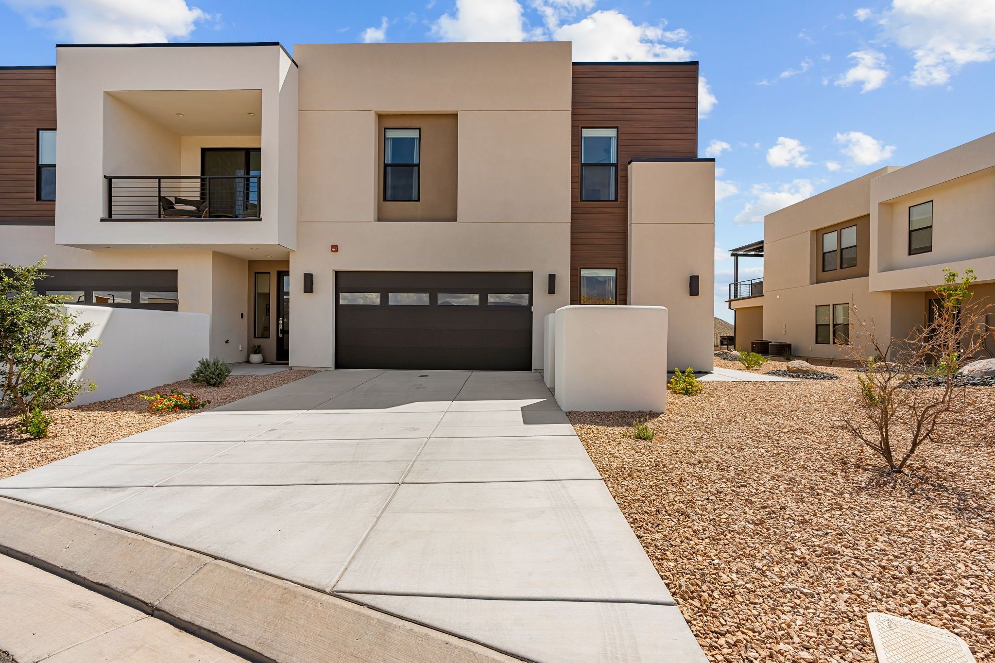 A modern multi-story residential building with a garage, a covered outdoor area, and a landscaped driveway.