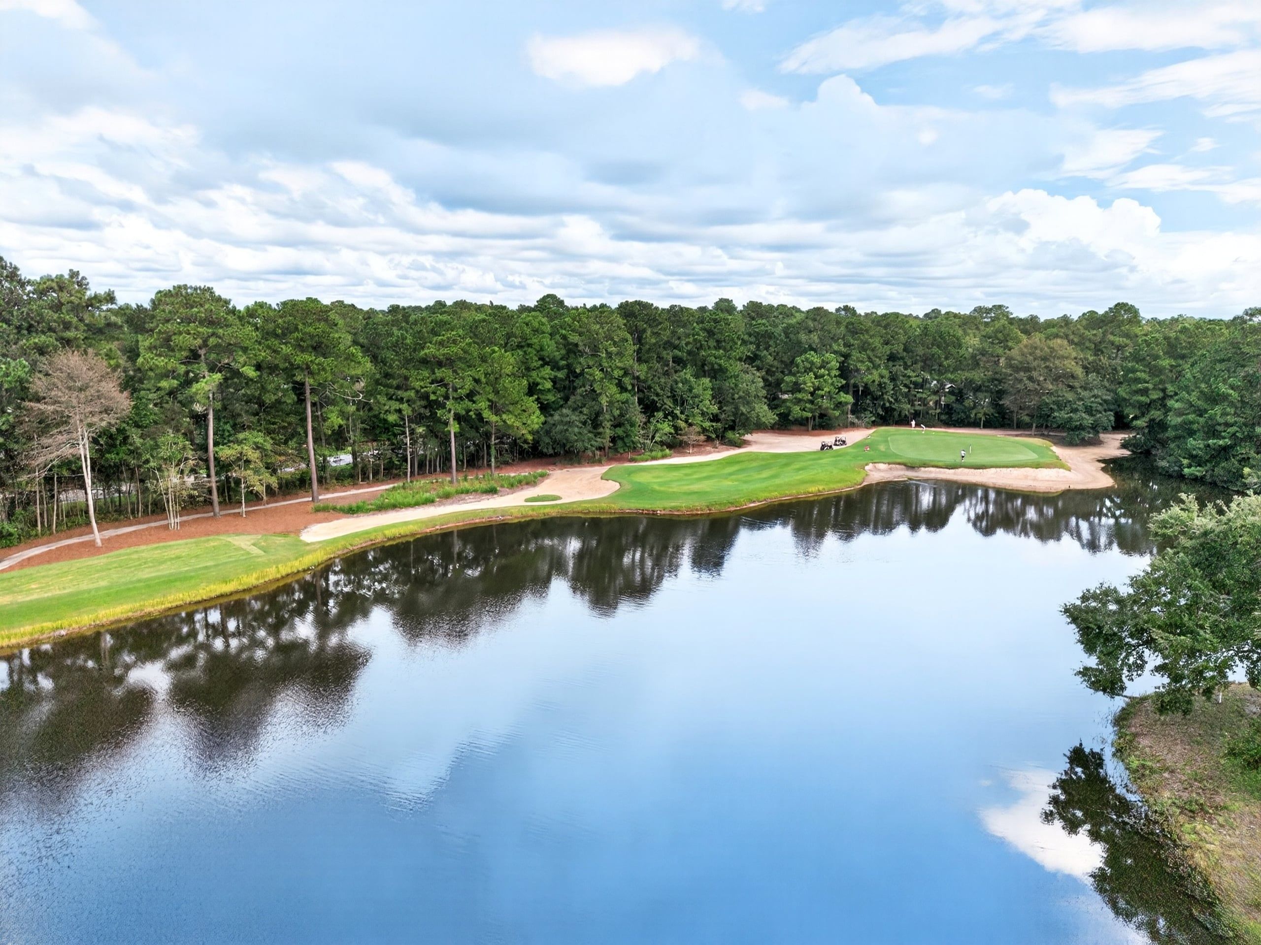 Un parcours de golf avec un étang, entouré d’arbres et sous un ciel dégagé.