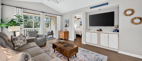 A spacious living room with a large sofa, a coffee table, and a television mounted on a white wall.