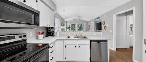 A modern kitchen with white cabinets, a stainless steel dishwasher, and a black microwave.