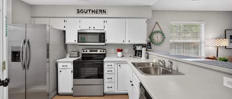 A modern kitchen with white cabinetry, stainless steel appliances, a built-in oven, microwave, and a sink with a faucet.