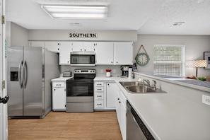 A modern kitchen with white cabinetry, stainless steel appliances, a built-in oven, microwave, and a sink with a faucet. - 6e Palmetto Paradise 2 Bedroom Condo (Pawleys Island)
