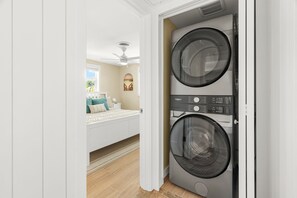 A laundry room with two stacked front-loading washers and dryers, a bed with a view of the outdoors, and a ceiling fan. - Siesta Time 4 Bedroom Home (Siesta Key)
