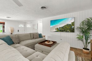 A modern living room with a sectional sofa, a coffee table, and a large TV mounted on the wall. - Siesta Time 4 Bedroom Home (Siesta Key)