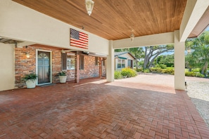 A covered patio with a brick floor, a brick wall, and a hanging American flag. - Siesta Time 4 Bedroom Home (Siesta Key)