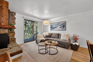 A modern living room with a stone fireplace, a sofa, a coffee table, and a painting on the wall. - Beaver Village unit 1811 renovated 2 bedroom, views from private deck, clubhouse (Winter Park)