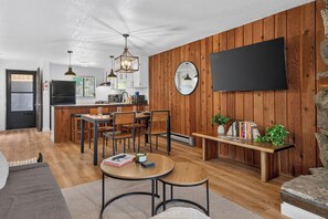 A modern kitchen with wooden paneling, a dining area with a round table, and a flat-screen TV mounted on the wall. - Beaver Village unit 1811 renovated 2 bedroom, views from private deck, clubhouse (Winter Park)