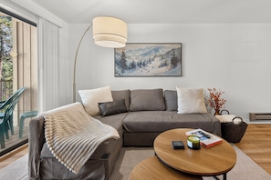 A modern living room with a grey sofa, a wooden coffee table, and a painting of a snowy landscape on the wall. - Beaver Village unit 1811 renovated 2 bedroom, views from private deck, clubhouse (Winter Park)