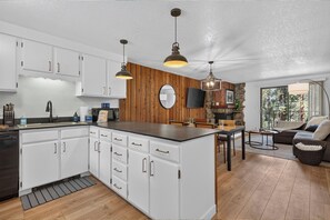 A modern kitchen with white cabinetry, a wooden accent wall, and pendant lighting. - Beaver Village unit 1811 renovated 2 bedroom, views from private deck, clubhouse (Winter Park)
