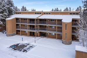 Ein mehrstöckiges Gebäude mit Balkonen, einem Parkplatz und schneebedeckten Bäumen.