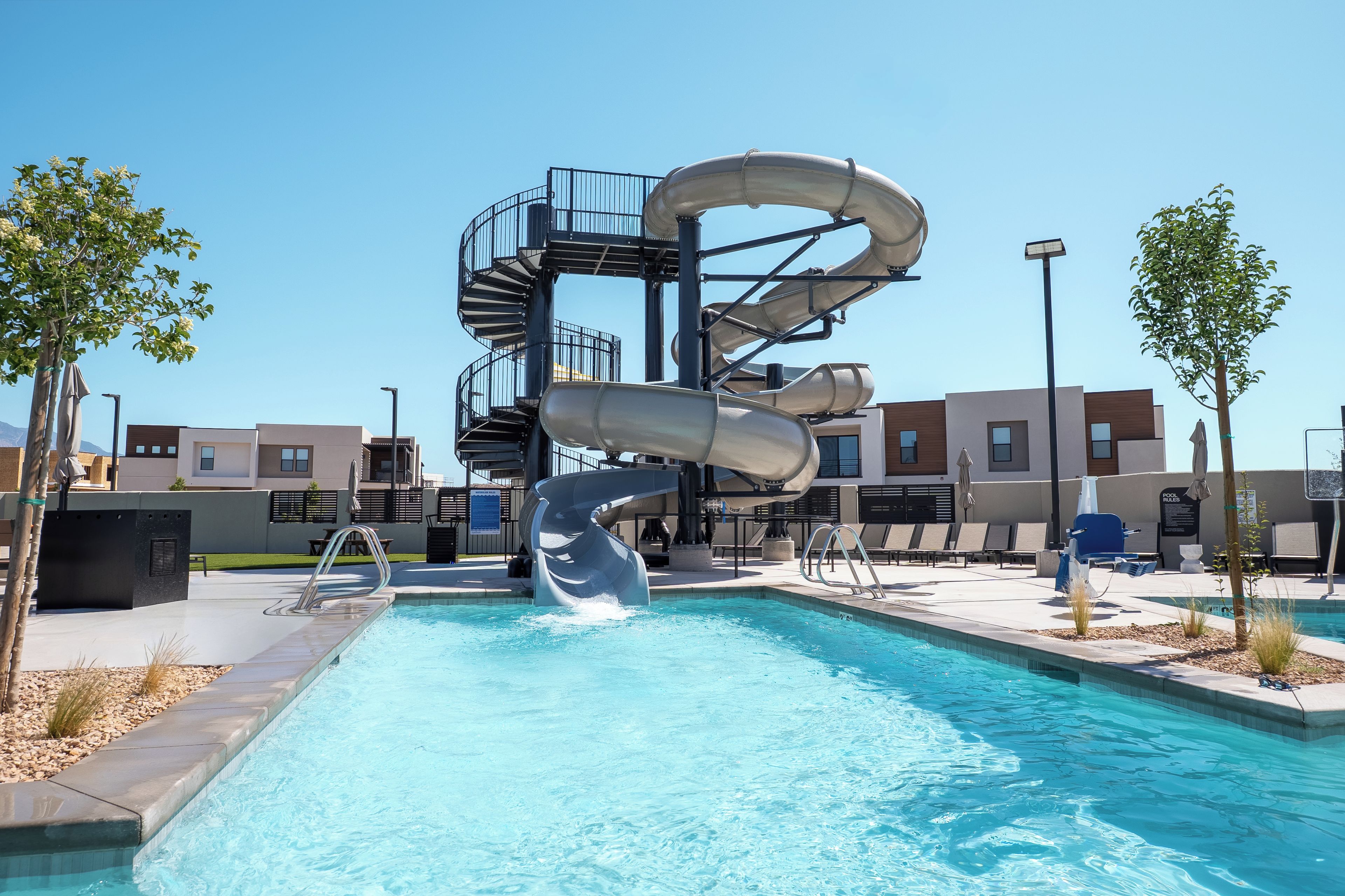 A swimming pool with a water slide, surrounded by modern buildings and a clear sky.