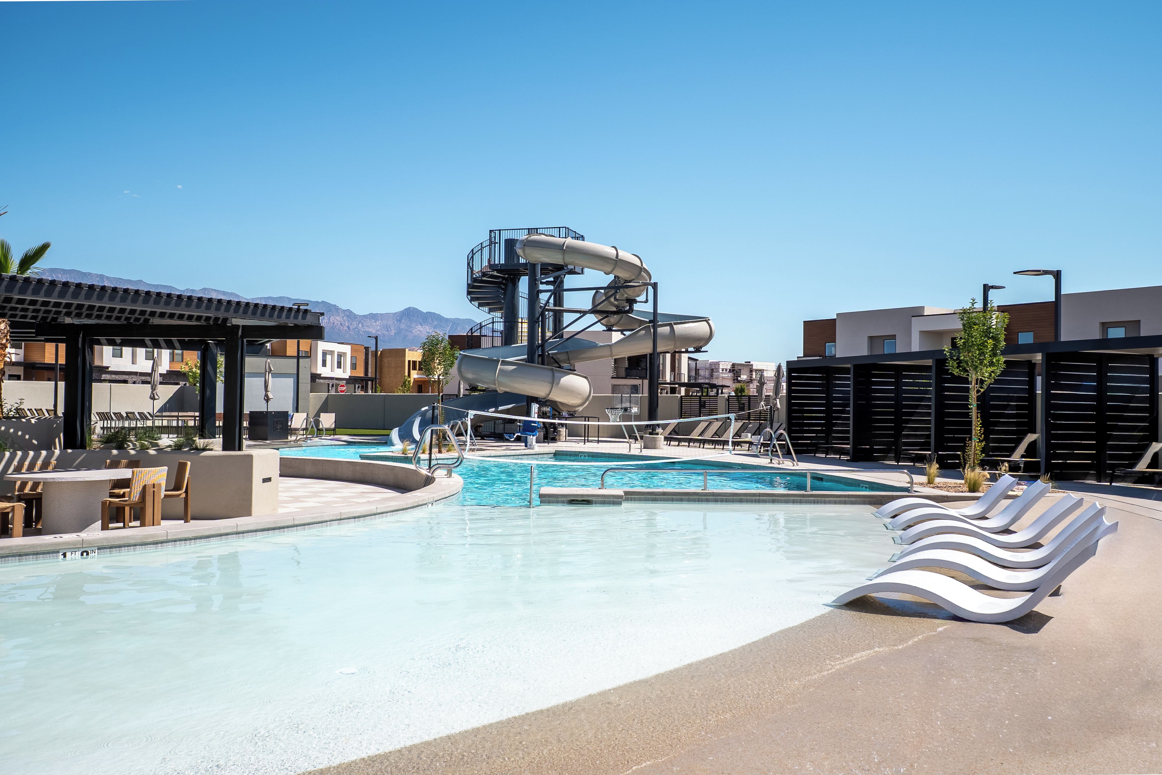 A swimming pool with a water slide, lounge chairs, and a mountain view.