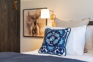 Ein Hotelzimmer mit einem Bett, einem Zierkissen, einer Wandlampe und einem Bild von einem Reh in einem Bilderrahmen.