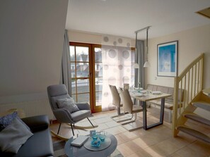 A modern living room with a sofa, a rocking chair, a dining table set for four, and a staircase. - 3.6/t3 Holiday Home Park \"freesenbruch\" (Zingst)