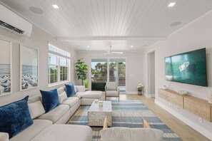 A modern living room with a sectional sofa, a coffee table, a TV, and a balcony with glass doors. - Luxury Pet Friendly Waterfront Home Private Pool & Dock in Resort Community Manatee Dreams at Hunters Point (Cortez)