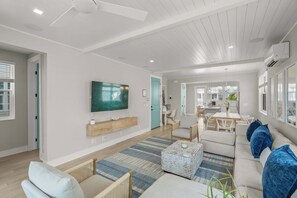A modern living room with a flat-screen TV, a wooden TV stand, a dining area with a table and chairs, and a kitchen in the background. - Luxury Pet Friendly Waterfront Home Private Pool & Dock in Resort Community Manatee Dreams at Hunters Point (Cortez)