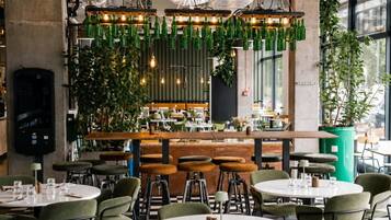 Ein Restaurant mit runden Tischen, Barhocker, hängenden grünen Flaschen und Zimmerpflanzen.
