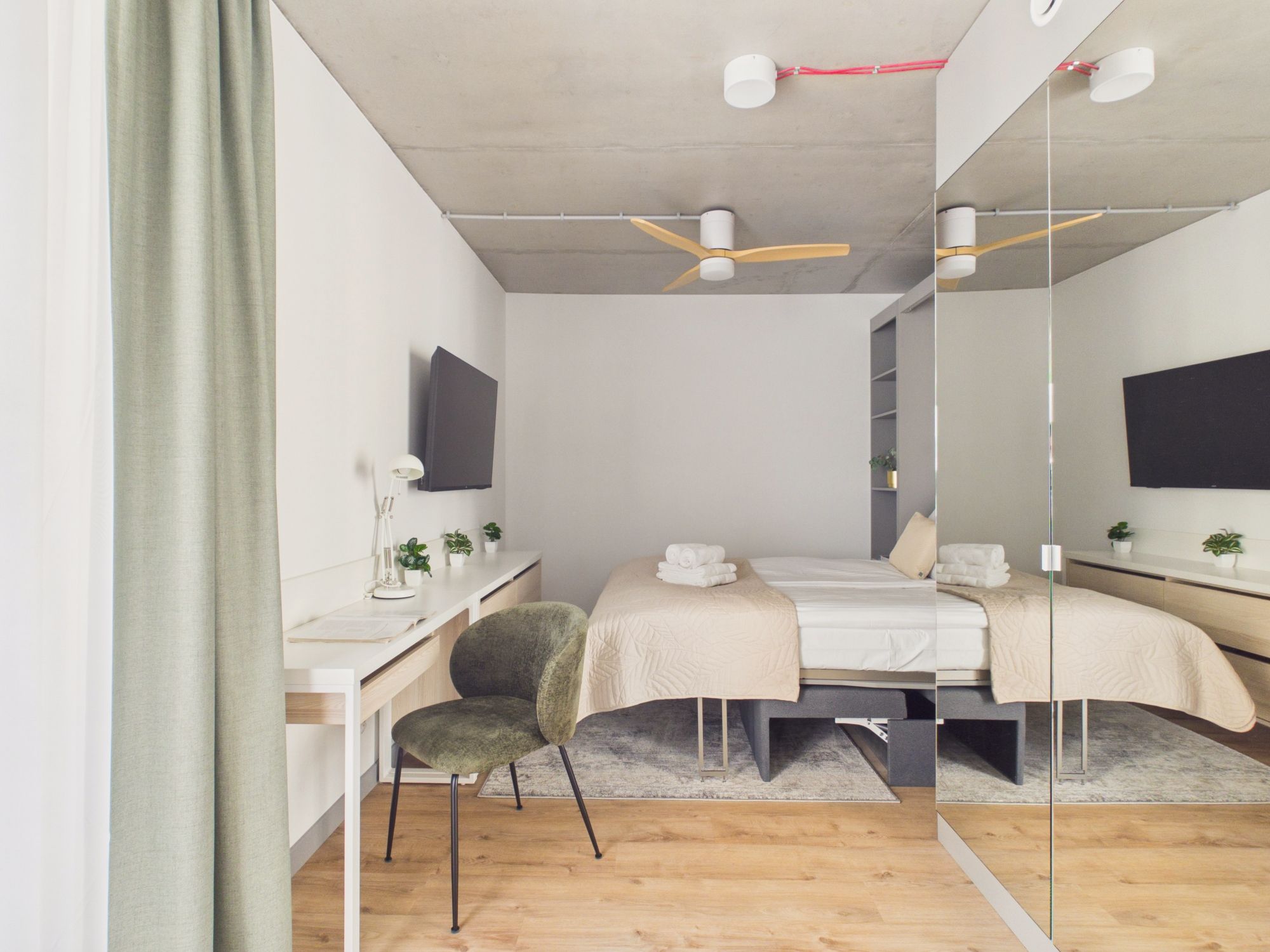 A modern bedroom with a desk, two beds, a chair, and a large mirror.