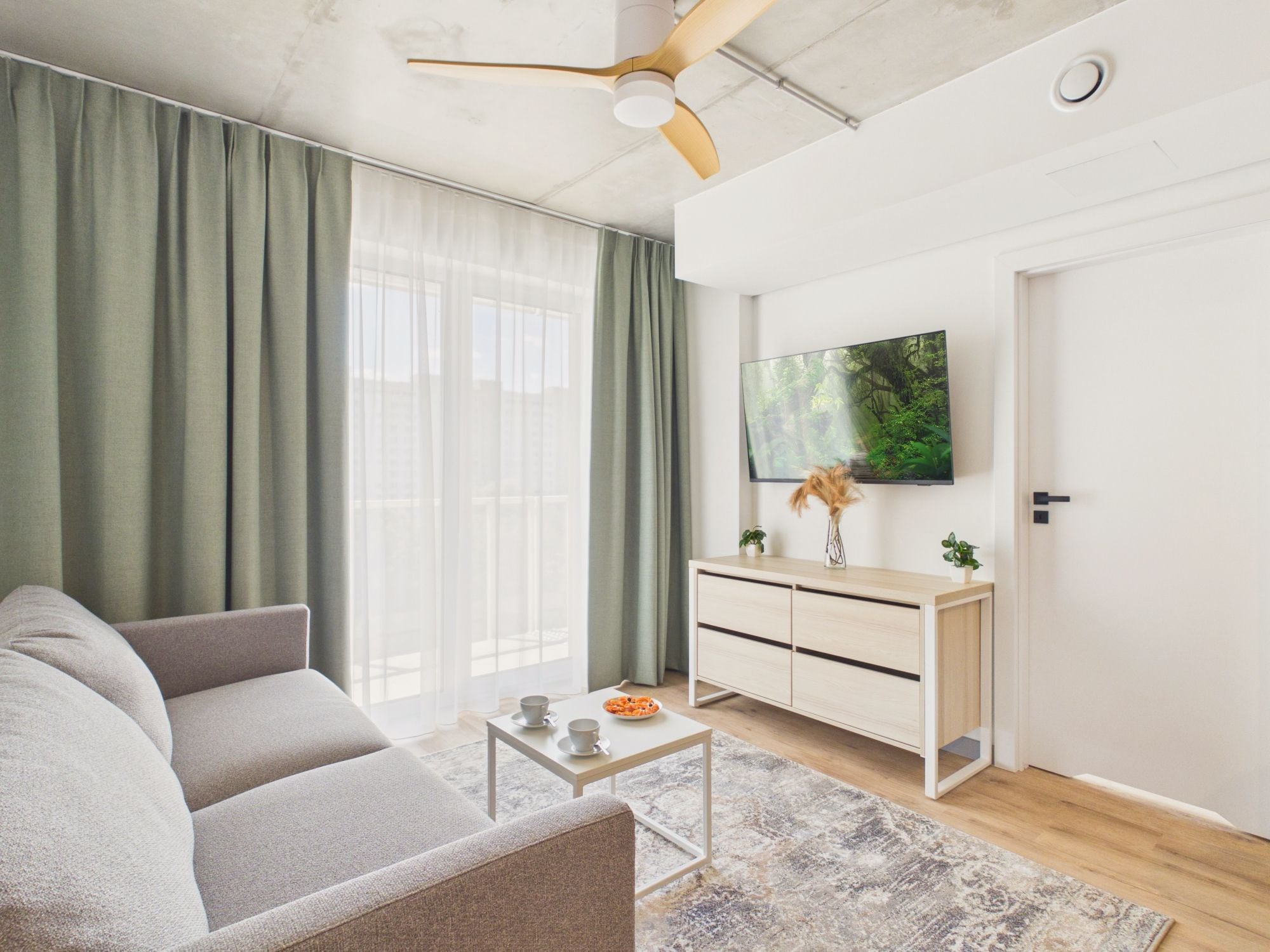 A modern living room with a sofa, a coffee table, a TV on the wall, and a door.