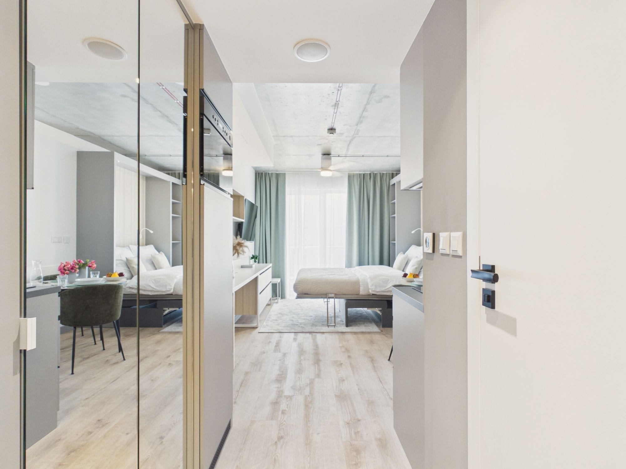 A modern hotel room with a bed, bedside table, and a desk with a chair.