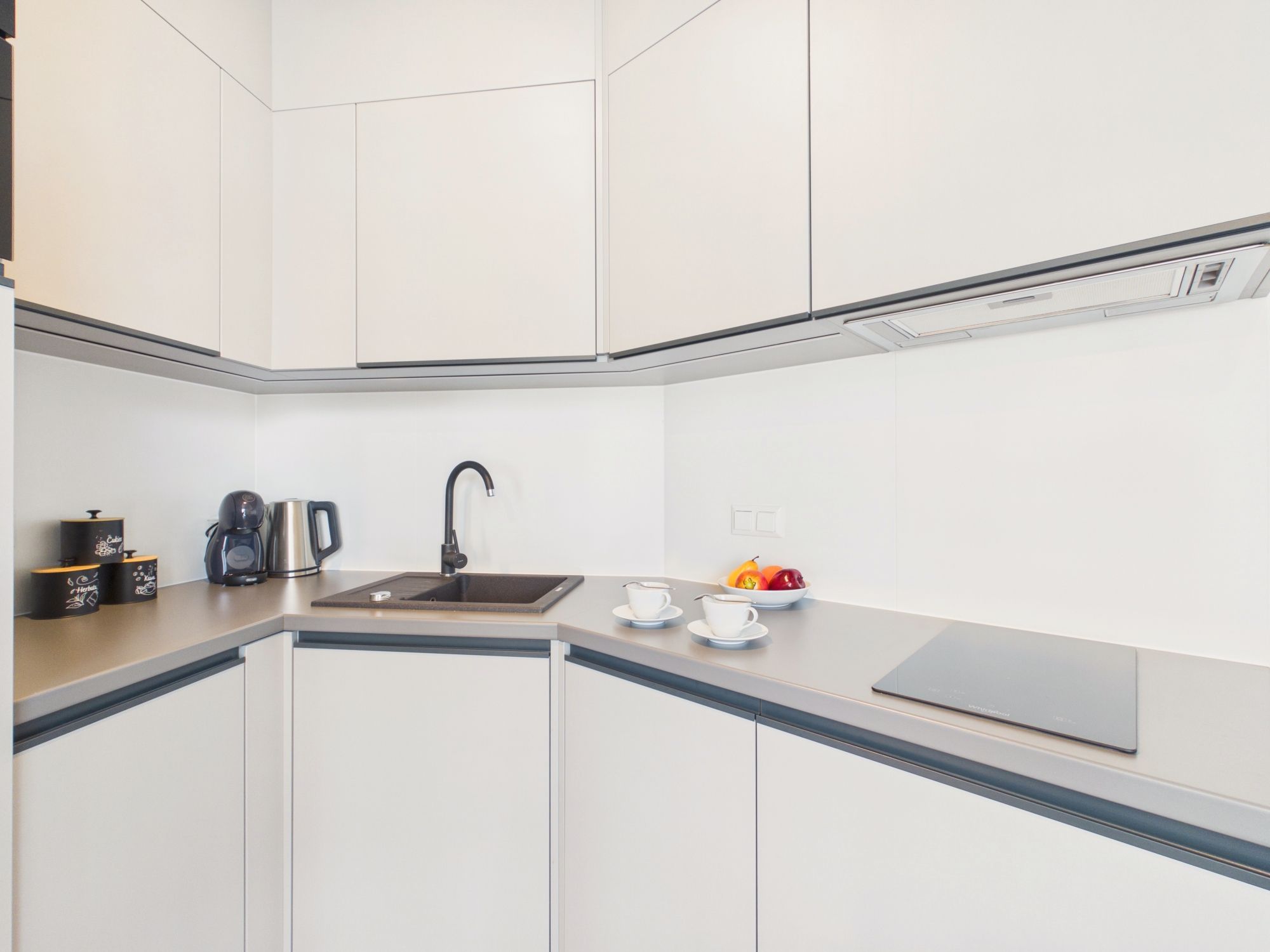 Een moderne keuken met witte kasten, een zwarte kraan, een koffiezetapparaat en een schaal fruit op het aanrecht.