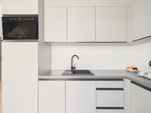 A modern kitchen with a built-in dishwasher, a stainless steel sink, and a fruit bowl on the countertop. - NanoApart by Solarento (Warszawa)