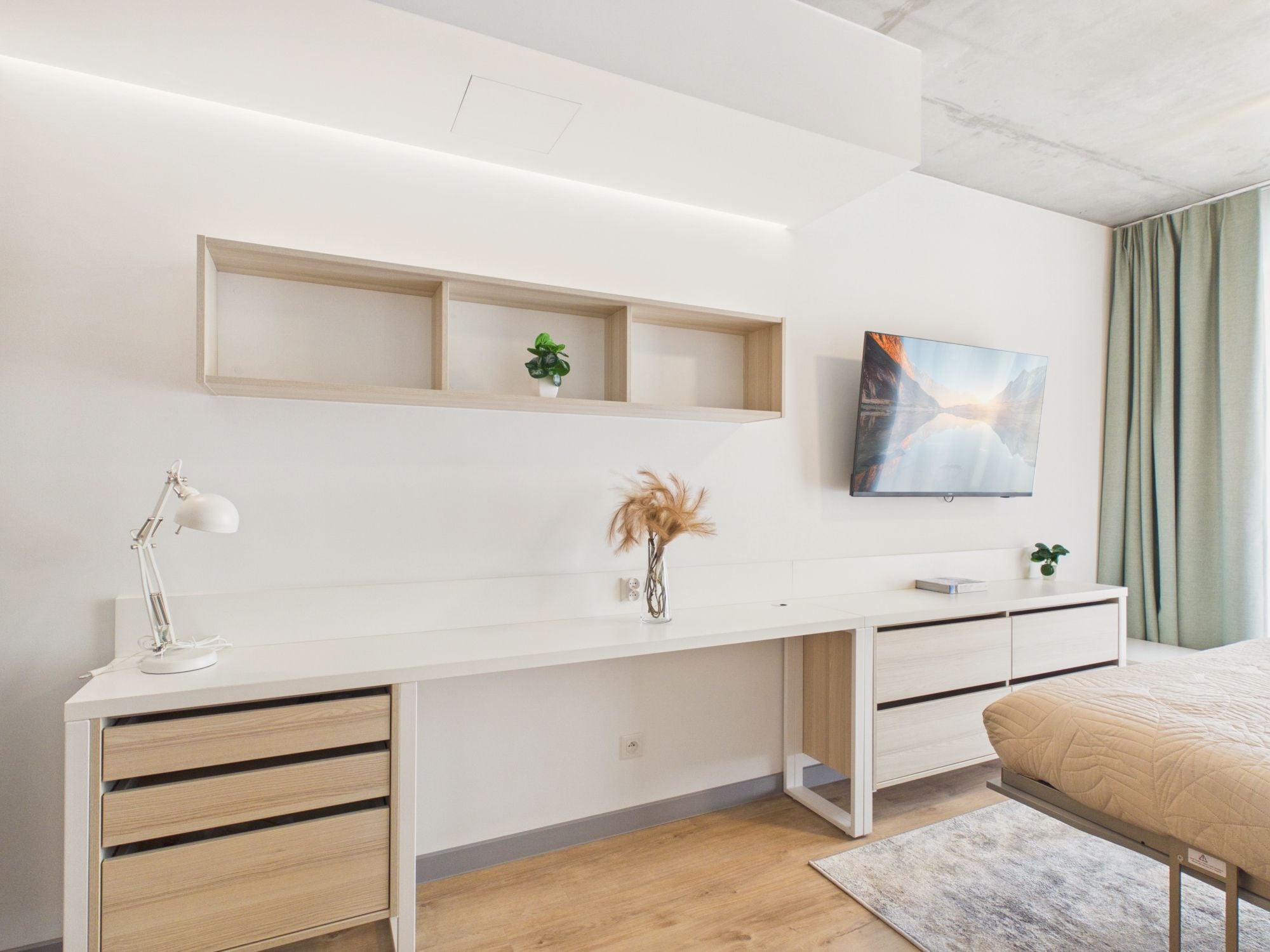 Una camera da letto moderna con una scrivania bianca, un letto, una TV a parete e una piccola pianta.
