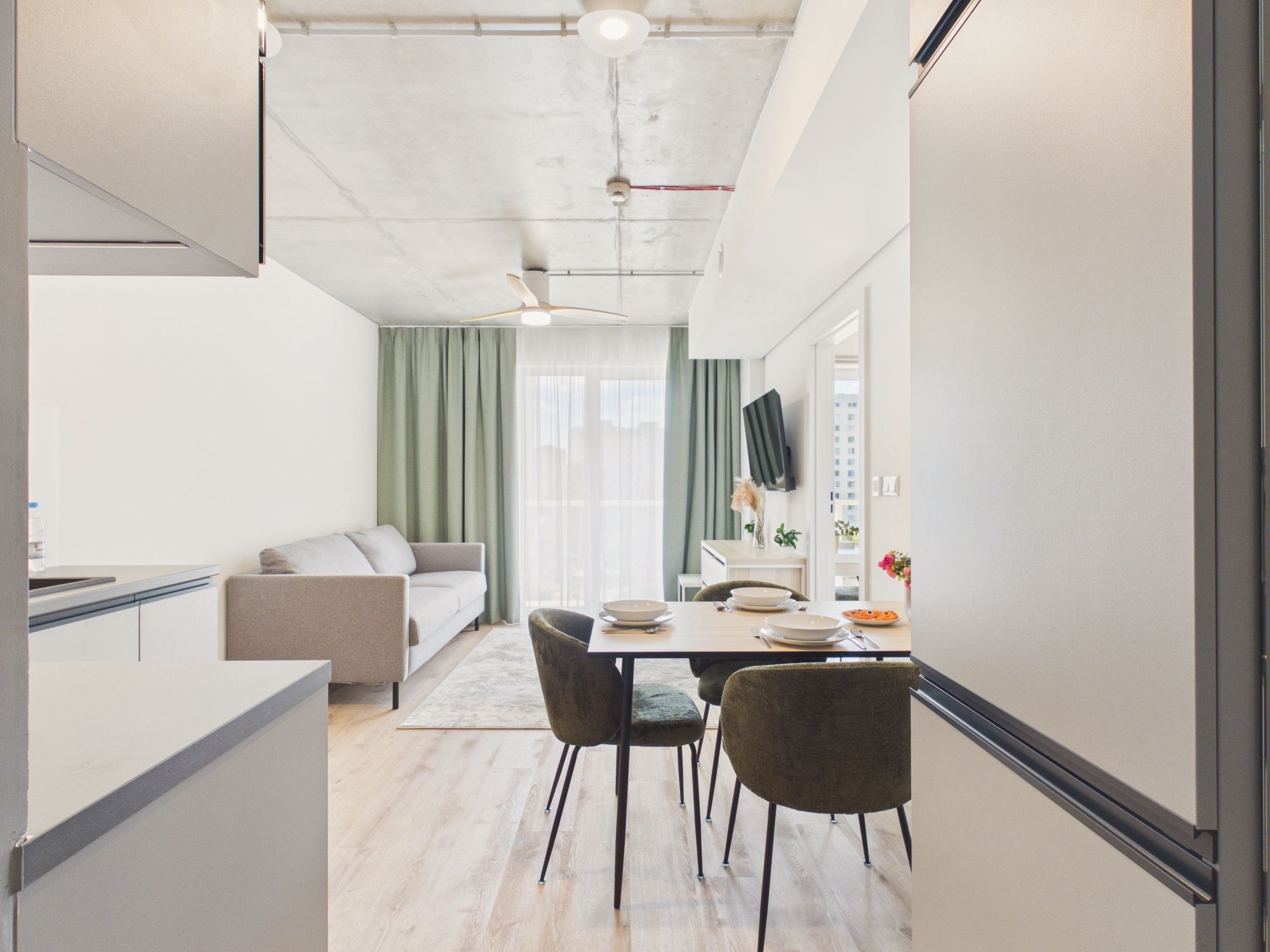 A modern kitchen with a dining area, a sofa, and a view of the city.