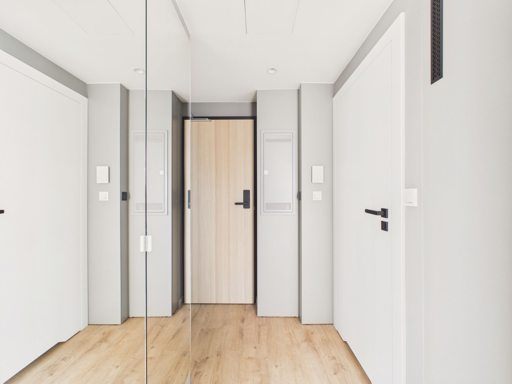 Un pasillo con paredes espejadas, una puerta de madera al final y un interruptor de luz en la pared.