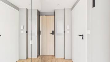 Un pasillo con paredes espejadas, una puerta de madera al final y un interruptor de luz en la pared.