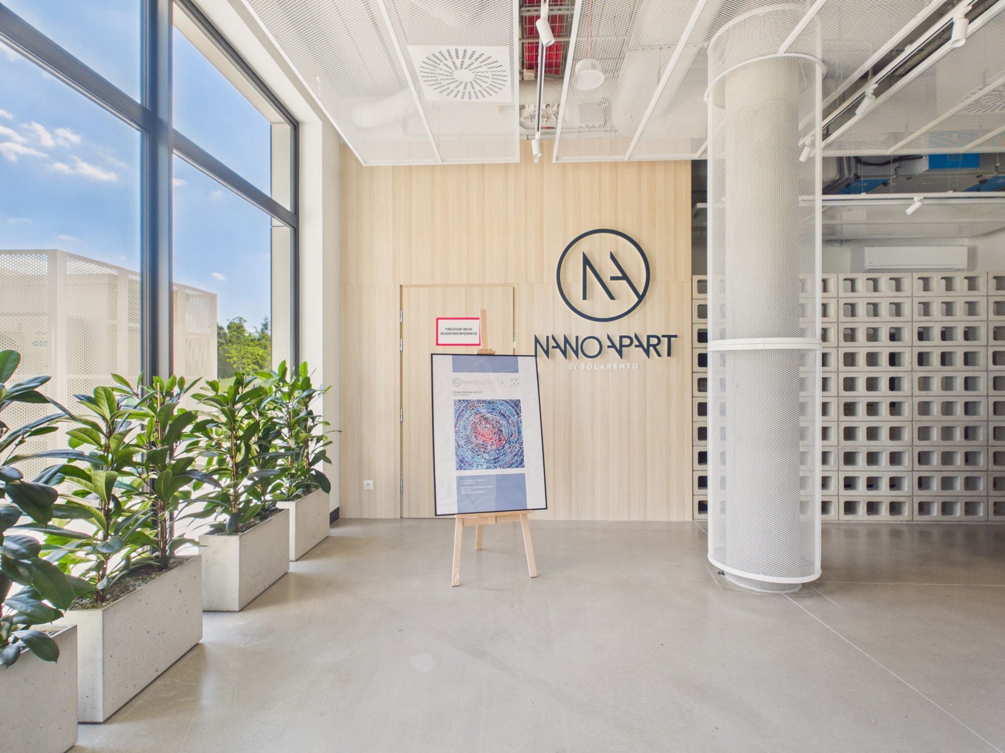 A modern interior with a large window, a wall-mounted sign reading 'NANO PART', and a framed artwork on easels.