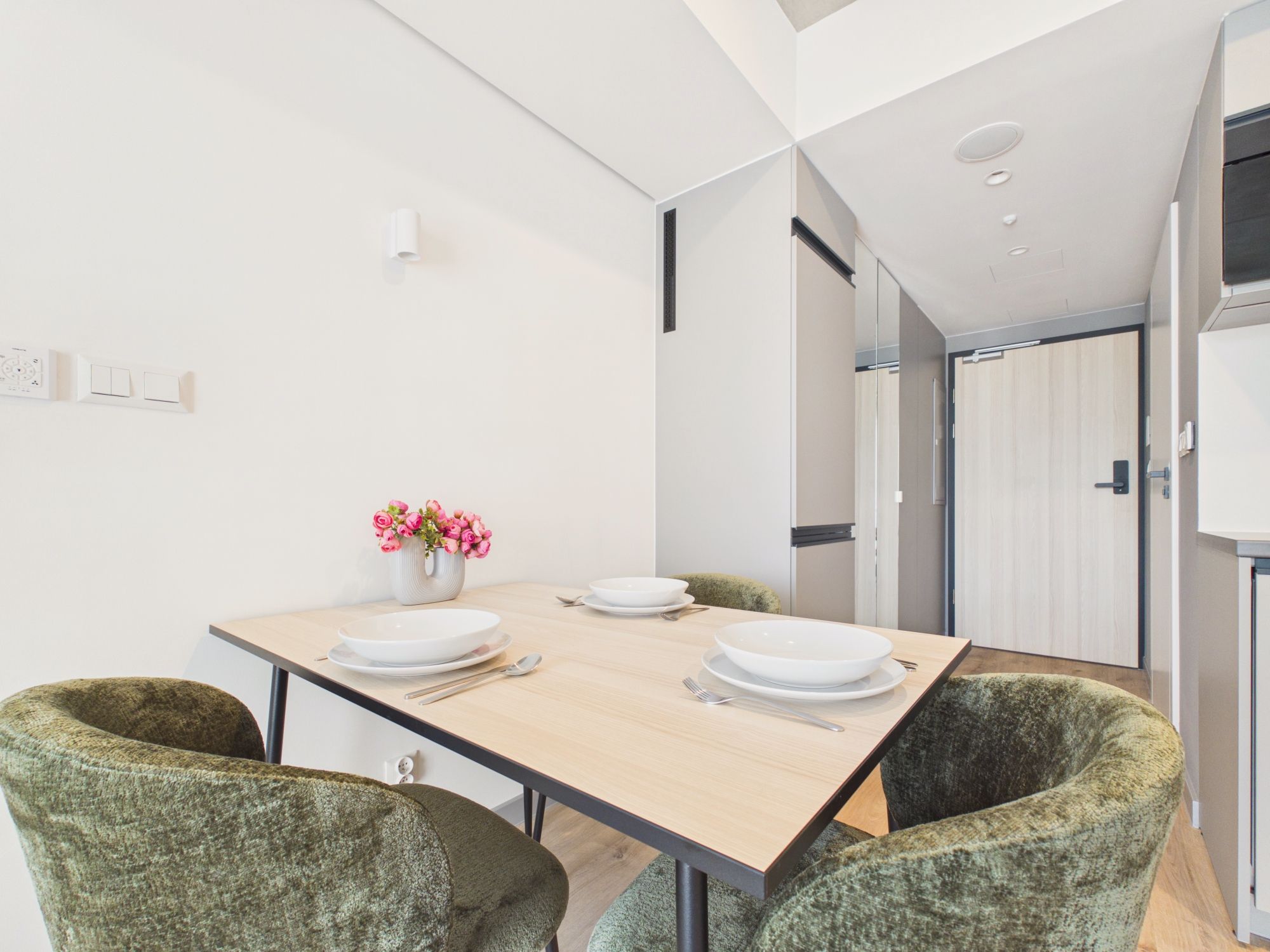 A modern dining area with a wooden table, two chairs, and a vase of flowers.